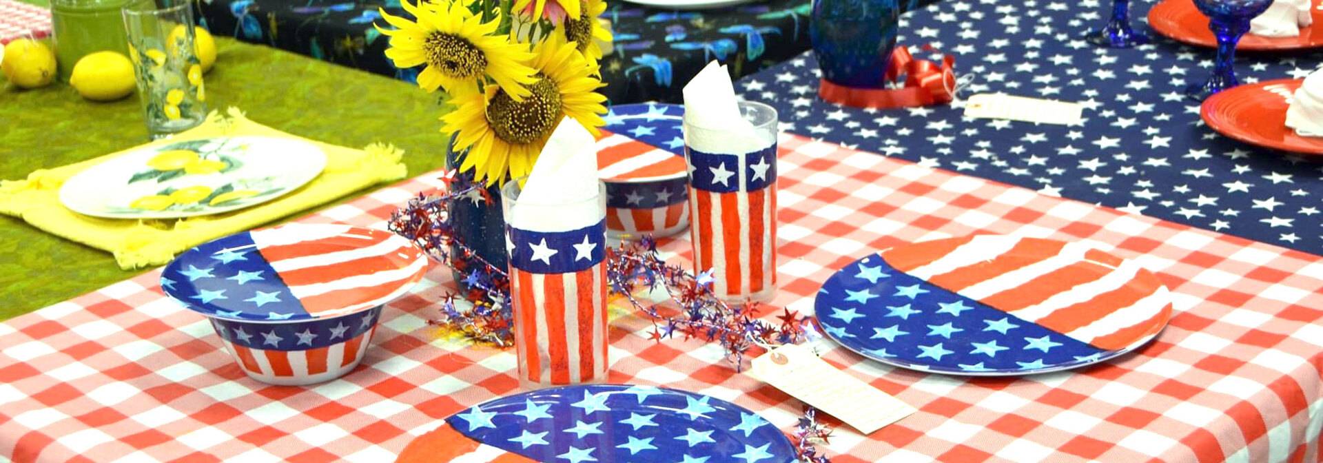 Patriotic table setting with red & white checkered tablecloth and plates and cups with American flag pattern